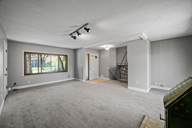 unfurnished living room featuring carpet floors, rail lighting, stairway, a textured ceiling, and baseboards
