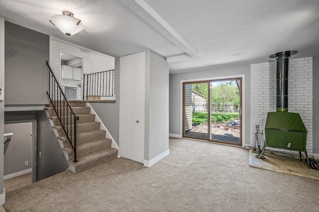 unfurnished living room featuring a textured ceiling, a wood stove, carpet floors, stairs, and baseboards