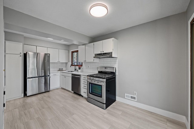 kitchen featuring stainless steel appliances, under cabinet range hood, light countertops, decorative backsplash, and white cabinetry