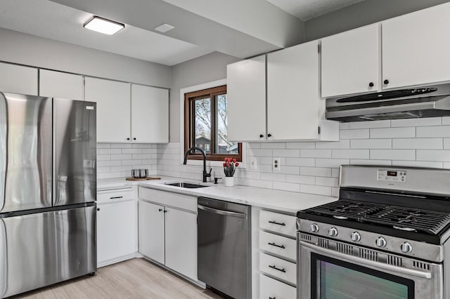 kitchen with appliances with stainless steel finishes, under cabinet range hood, a sink, white cabinetry, and backsplash