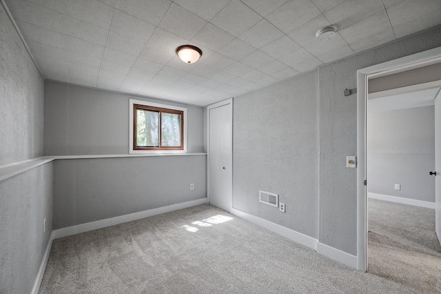 carpeted empty room featuring a textured wall and a smoke detector