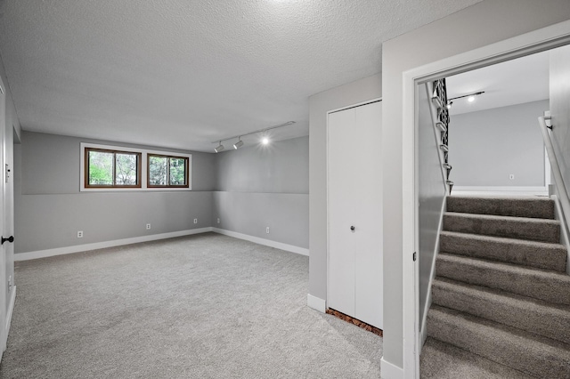 below grade area with carpet flooring, rail lighting, a textured ceiling, stairs, and baseboards