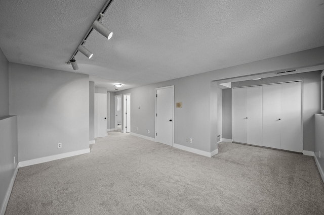 below grade area featuring a textured ceiling, track lighting, carpet floors, and baseboards