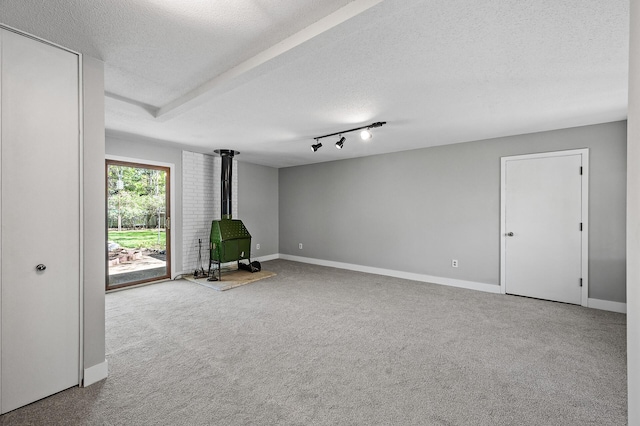 empty room featuring a wood stove, a textured ceiling, carpet, and baseboards