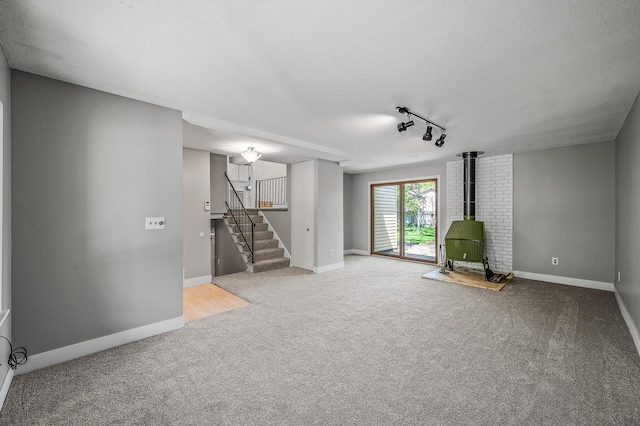 unfurnished room featuring a wood stove, carpet floors, stairs, and baseboards