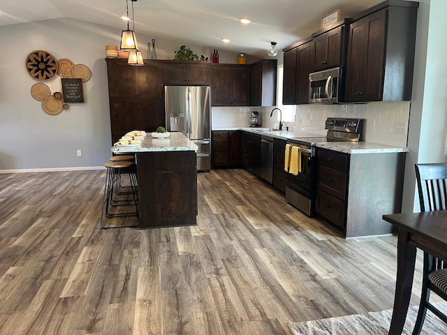 kitchen with dark brown cabinetry, tasteful backsplash, a sink, appliances with stainless steel finishes, and vaulted ceiling
