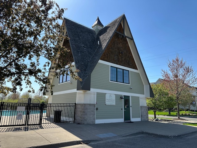 view of front of property with fence, a shingled roof, and a swimming pool