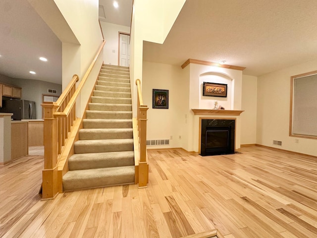 stairway featuring wood finished floors, recessed lighting, a fireplace with flush hearth, and baseboards