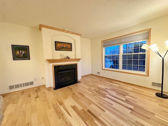 unfurnished living room featuring wood finished floors, a premium fireplace, baseboards, and a textured ceiling
