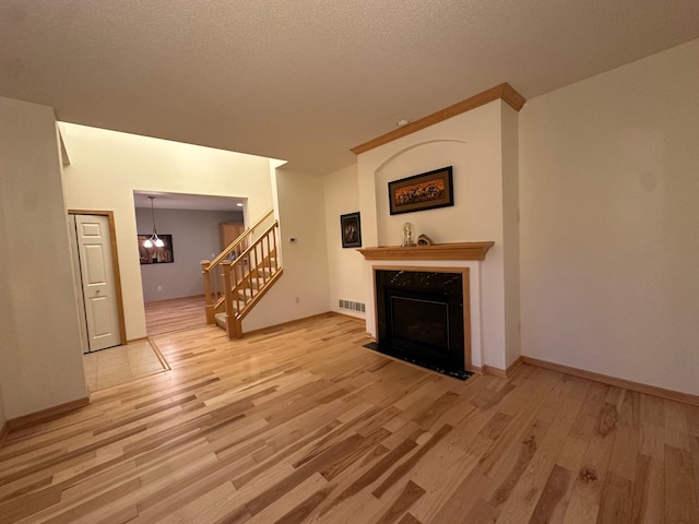 unfurnished living room with stairs, light wood-style flooring, a fireplace, baseboards, and a textured ceiling