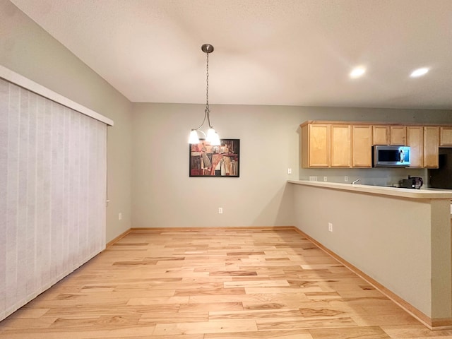 kitchen with stainless steel microwave, light brown cabinets, light wood-type flooring, light countertops, and baseboards