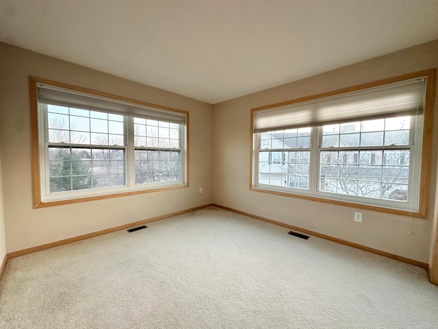 carpeted spare room with plenty of natural light, baseboards, and visible vents