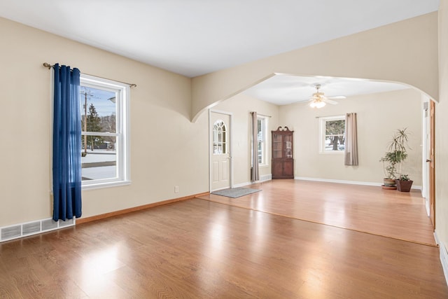 unfurnished living room with arched walkways, wood finished floors, ceiling fan, baseboards, and visible vents