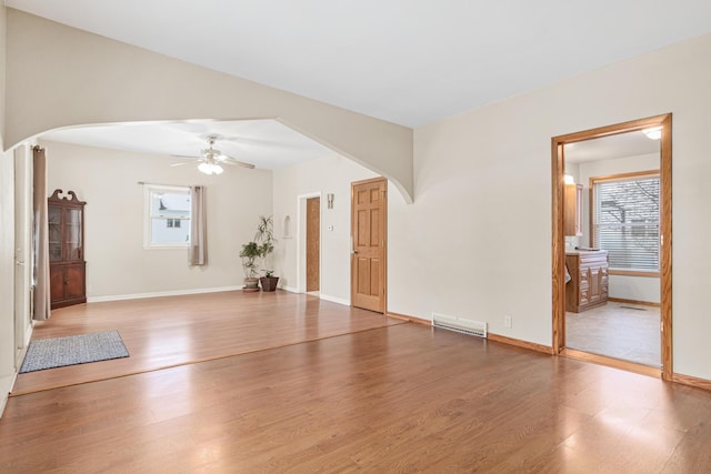 unfurnished living room featuring arched walkways, a wealth of natural light, wood finished floors, and ceiling fan