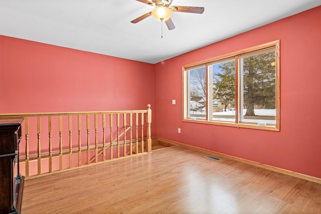 unfurnished room featuring a ceiling fan, visible vents, wood finished floors, and baseboards
