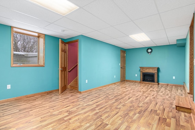 unfurnished living room featuring baseboards, a drop ceiling, wood finished floors, and a fireplace