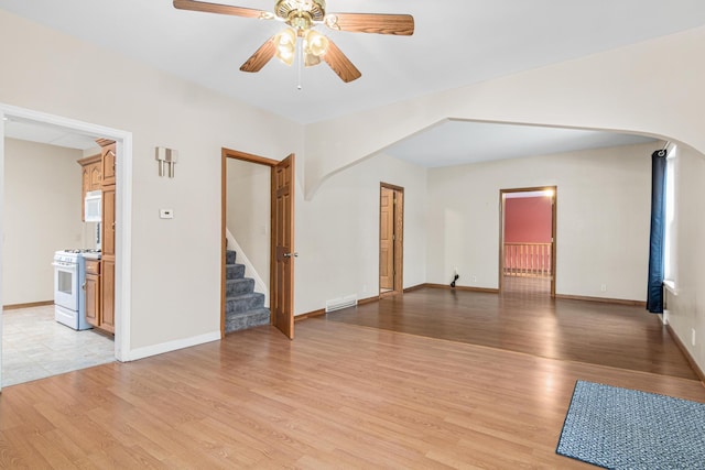 unfurnished living room with stairway, ceiling fan, visible vents, arched walkways, and light wood-type flooring
