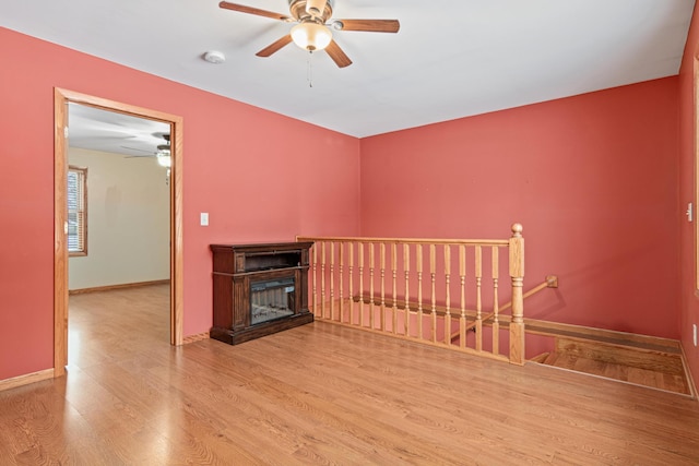 empty room featuring a ceiling fan, baseboards, wood finished floors, and a fireplace