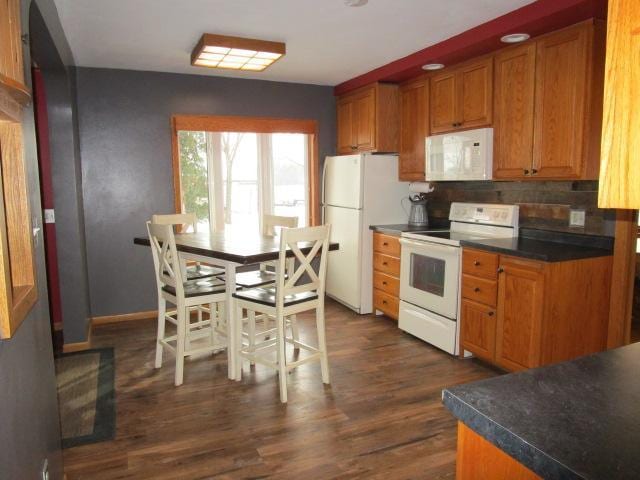 kitchen featuring white appliances, brown cabinetry, dark wood-type flooring, and dark countertops