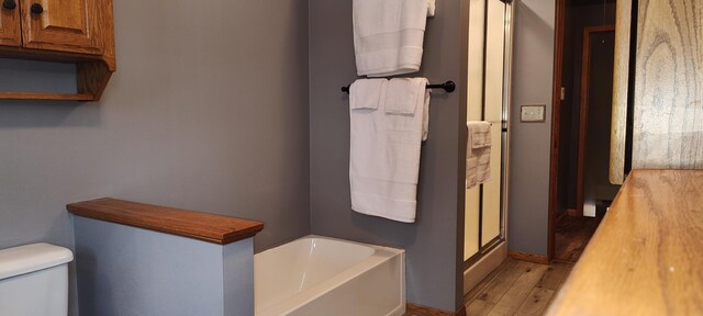 bathroom with a bath, wood finished floors, toilet, and a stall shower