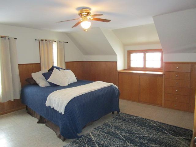 bedroom with wood walls, lofted ceiling, a wainscoted wall, and ceiling fan