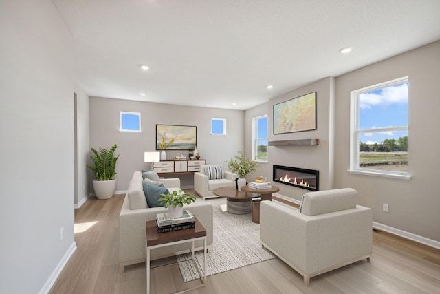 living room with a glass covered fireplace, light wood finished floors, recessed lighting, and baseboards