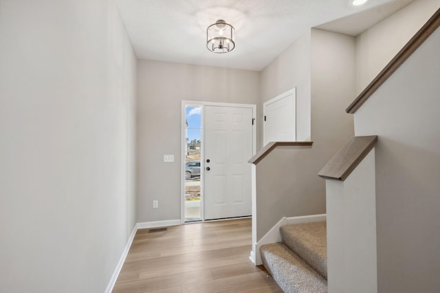 foyer featuring stairway, wood finished floors, baseboards, and a chandelier