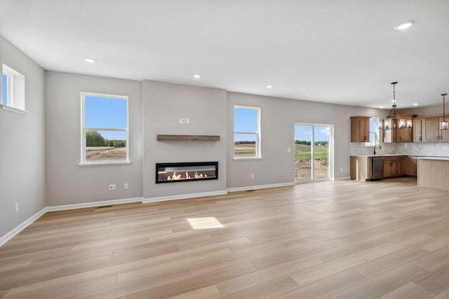 unfurnished living room featuring recessed lighting, a chandelier, a glass covered fireplace, light wood-style flooring, and baseboards