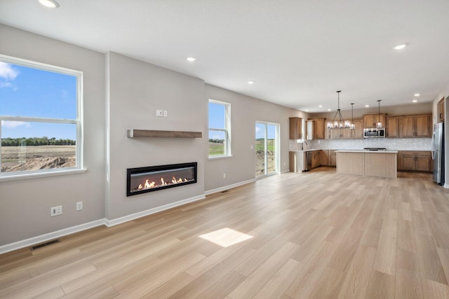 unfurnished living room with recessed lighting, a glass covered fireplace, a chandelier, light wood finished floors, and baseboards