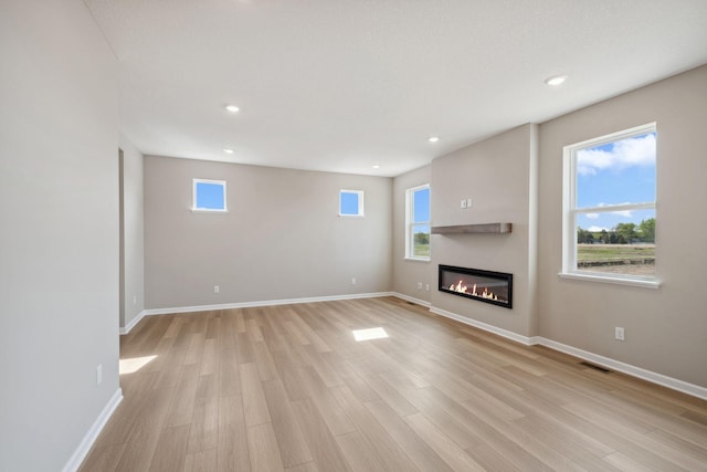 unfurnished living room featuring a glass covered fireplace, recessed lighting, light wood-style flooring, and baseboards