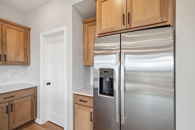 kitchen with stainless steel fridge with ice dispenser, decorative backsplash, light countertops, and light wood-type flooring
