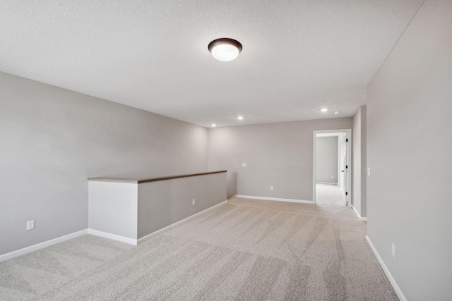 empty room with light carpet, recessed lighting, baseboards, and a textured ceiling