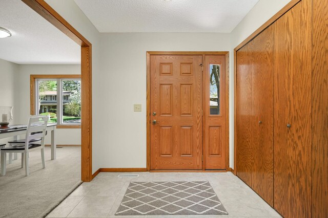 foyer entrance featuring baseboards, a textured ceiling, and light colored carpet