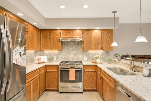 kitchen featuring appliances with stainless steel finishes, a sink, decorative backsplash, light stone counters, and hanging light fixtures
