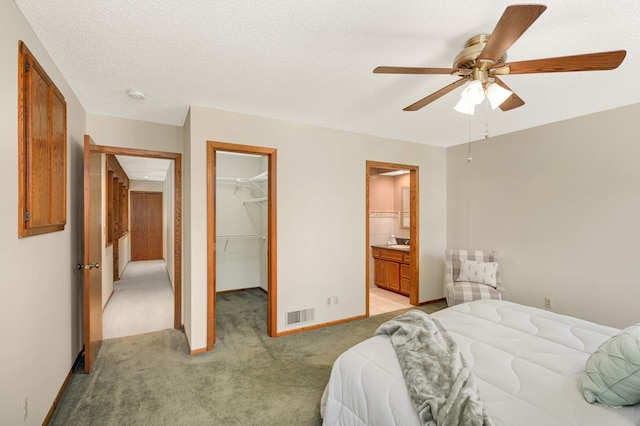 bedroom with light colored carpet, a spacious closet, a closet, a ceiling fan, and ensuite bath