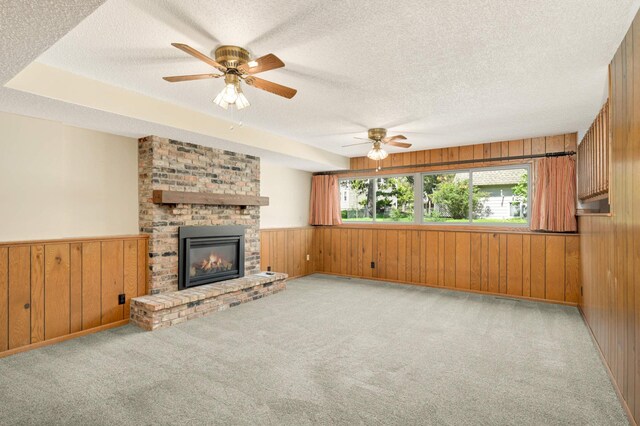 unfurnished living room featuring wood walls, a textured ceiling, carpet, a fireplace, and ceiling fan