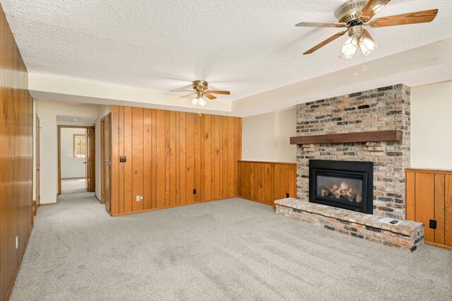 unfurnished living room featuring a ceiling fan, carpet, a textured ceiling, a fireplace, and wood walls