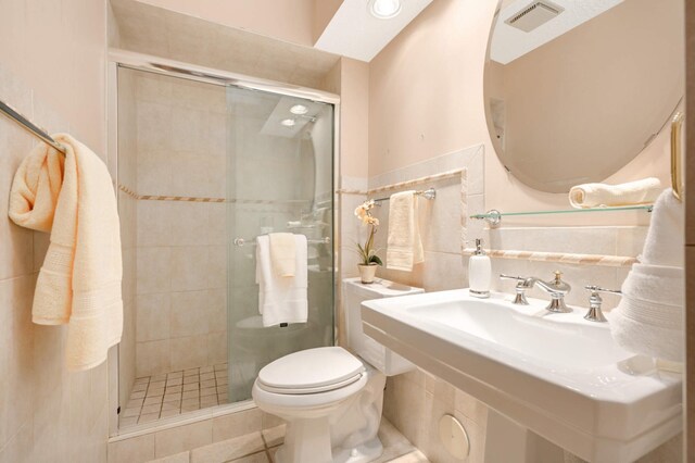 full bath featuring tile walls, a stall shower, toilet, tile patterned floors, and a wainscoted wall