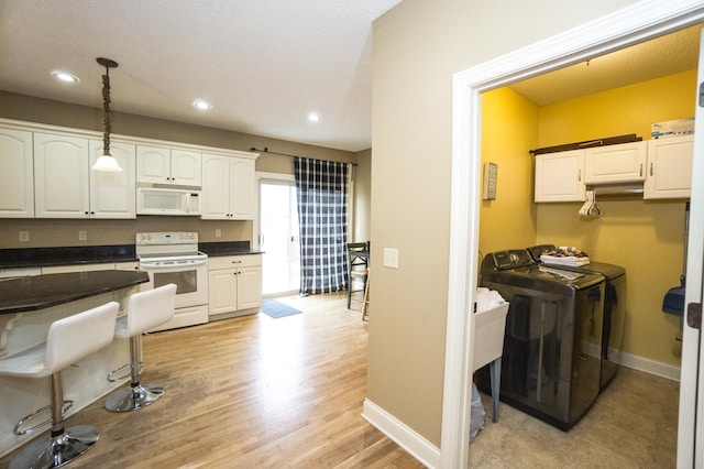 11474 Laketowne Dr, Albertville, MN 55301 - kitchen with white appliances, washing machine and clothes dryer, dark countertops, white cabinetry, and decorative light fixtures