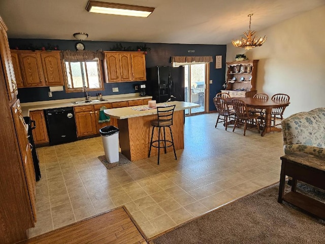 kitchen featuring black appliances, a center island, light countertops, a sink, and brown cabinets
