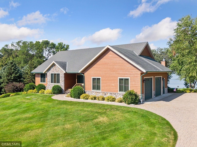 view of front of house with an attached garage, stone siding, decorative driveway, a front lawn, and a chimney