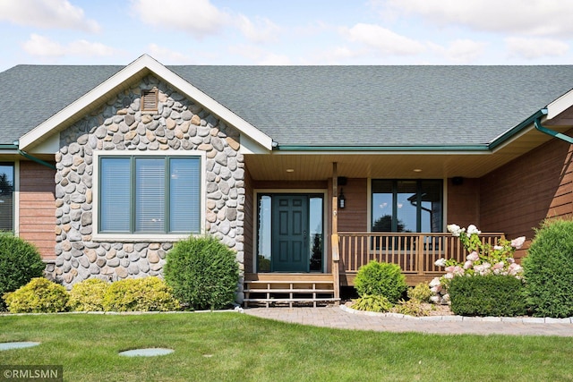 view of front facade featuring a front lawn, a shingled roof, and stone siding