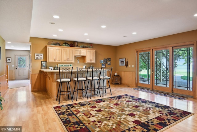 kitchen with recessed lighting, a breakfast bar, a wainscoted wall, light wood-style floors, and a peninsula