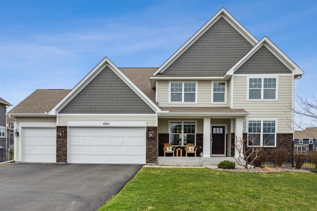 craftsman-style home featuring aphalt driveway, an attached garage, fence, a front yard, and a porch