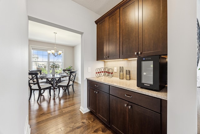 bar with a chandelier, decorative light fixtures, baseboards, decorative backsplash, and dark wood-style floors