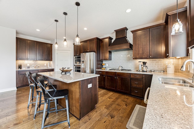 kitchen with custom exhaust hood, a center island, light stone counters, a sink, and appliances with stainless steel finishes