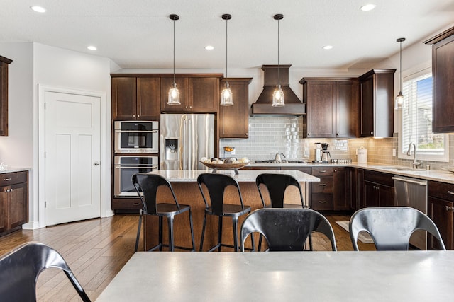 kitchen featuring a breakfast bar area, dark wood-style floors, premium range hood, a sink, and stainless steel appliances