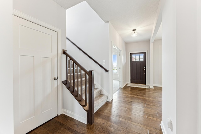 foyer with dark wood-type flooring, baseboards, and stairs