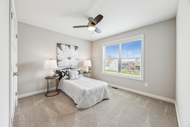 bedroom with a ceiling fan, a textured ceiling, visible vents, baseboards, and carpet flooring