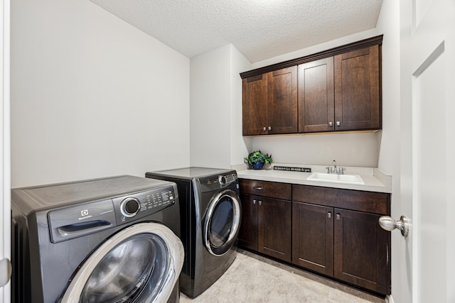 laundry area featuring cabinet space, a textured ceiling, washing machine and dryer, and a sink